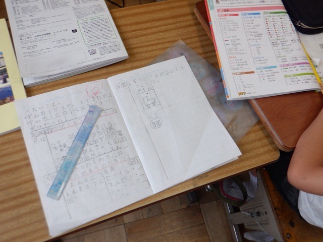 生徒の机の上に置かれたノートと文房具。ノートには地図記号の説明とオリジナルの地図記号が描かれている。
